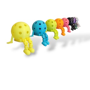 Pu&ograve; includere: Una fila di figurine colorate e stravaganti in una variet&agrave; di colori, tra cui giallo, blu, verde, arancione, rosa, nero e viola. Ogni figurina ha una testa sferica con fori e arti articolati.