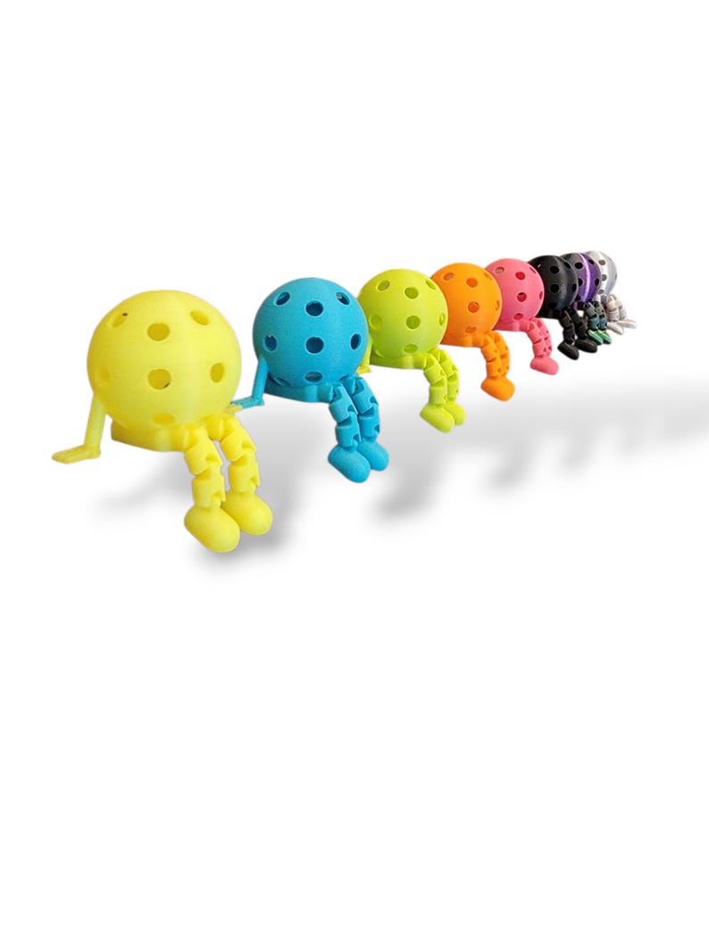 Pu&ograve; includere: Una fila di figurine colorate e stravaganti in una variet&agrave; di colori, tra cui giallo, blu, verde, arancione, rosa, nero e viola. Ogni figurina ha una testa sferica con fori e arti articolati.