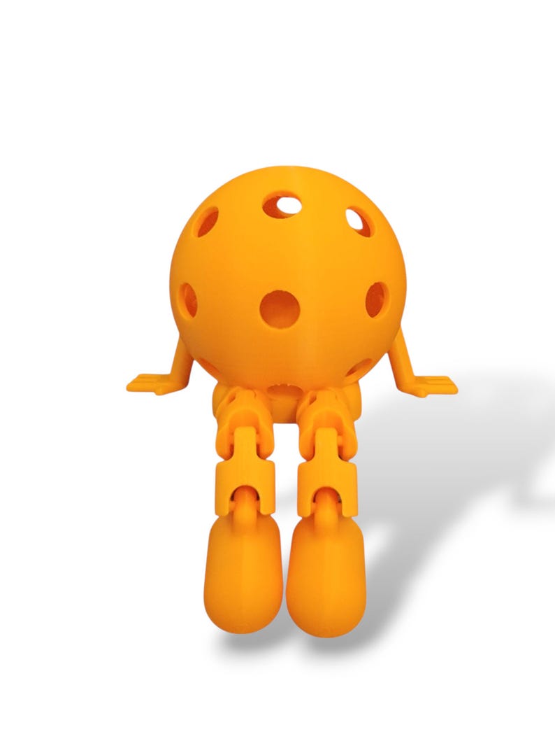 May include: A bright orange, spherical, 3D-printed toy with multiple circular holes. The toy has articulated legs and arms, giving it a playful appearance. The design is simple and modern, with a smooth, matte finish. The toy is sitting, with its legs dangling.