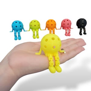Pu&ograve; includere: Una collezione di figurine colorate stampate in 3D, ciascuna con una testa sferica e gambe articolate. Le figurine sono in vari colori: blu, verde, arancione, rosa, giallo e nero. La figurina gialla &egrave; in primo piano, con le altre disposte dietro.