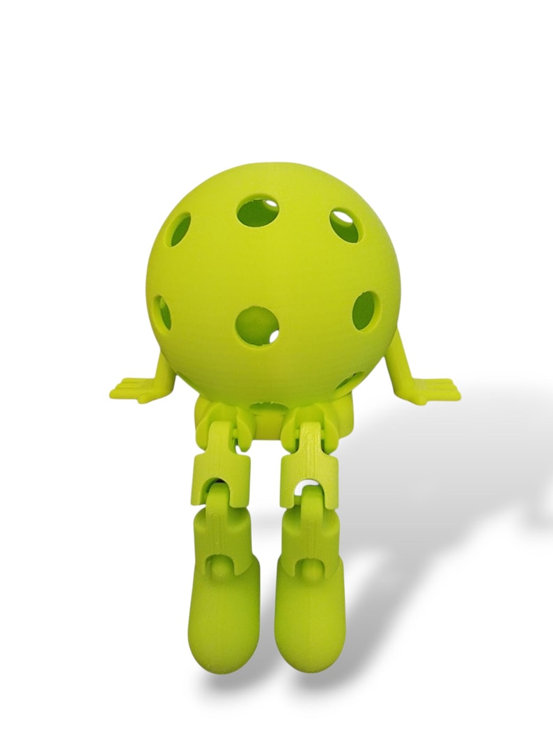 May include: A lime green, 3D-printed articulated ball figure with a spherical head featuring several circular holes. The figure has jointed legs and small, flat arms, giving it a playful, cartoonish appearance. The figure is set against a white background.