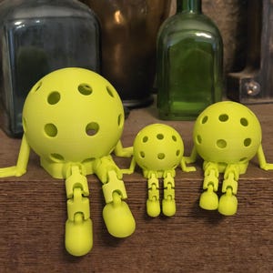 May include: Three lime green articulated figures with spherical heads featuring multiple circular cutouts. Each figure has jointed arms and legs that allow for sitting positions, with a large figure on the left, a small one in the center, and a medium one on the right.
