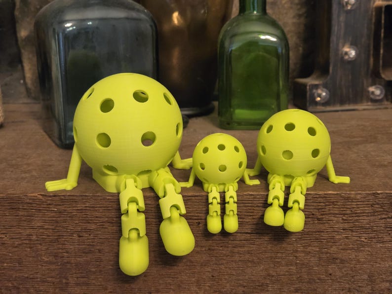 May include: Three lime green articulated figures with spherical heads featuring multiple circular cutouts. Each figure has jointed arms and legs that allow for sitting positions, with a large figure on the left, a small one in the center, and a medium one on the right.