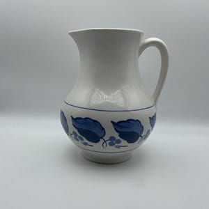 May include: A set of three ceramic canisters with lids. The canisters are white with a blue floral pattern. The largest canister is 8 inches tall, the medium is 7 inches, and the smallest is 6 inches.