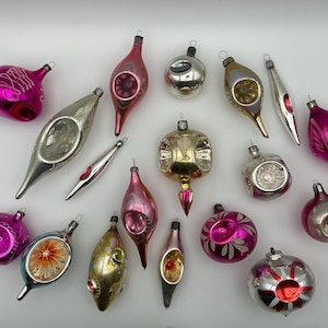 May include: A collection of vintage Christmas ornaments in various shapes and colors. The ornaments include silver, gold, pink, and red hues. Some have intricate designs and reflective surfaces, perfect for holiday decorating.
