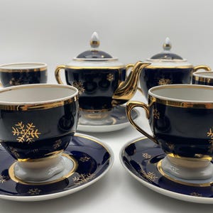 May include: A navy blue tea set with gold snowflake detailing. The set includes cups, saucers, a teapot, and a sugar bowl. Each piece has gold trim. The tea set is designed for serving tea and includes multiple cups and saucers.