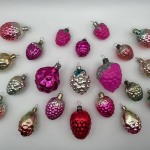 May include: A collection of twenty vintage glass ornaments shaped like berries and pinecones. The ornaments feature metallic, glossy, and matte finishes in shades of pink, magenta, gold, silver, and green, each topped with a small metal hanging loop.
