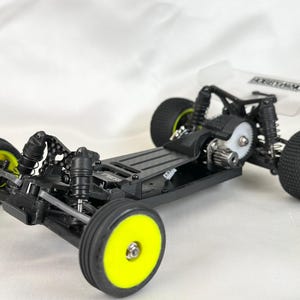 Peut inclure: Un châssis de voiture radiocommandée noir et jaune avec une carrosserie transparente et un moteur noir. La voiture a quatre roues avec des jantes jaunes et des pneus noirs.