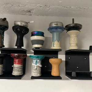 May include: A set of six black metal shelves with different colored ceramic and glass hookah bowls. The shelves are mounted on a wall.