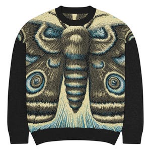 Puede incluir: Sudadera de cuello redondo con un diseño detallado de polilla. La polilla está representada en tonos beige, azul y marrón, con patrones intrincados. Las mangas y el cuello son de color negro liso.