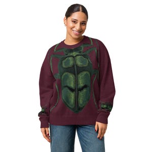 May include: A maroon long-sleeve sweatshirt featuring a large, detailed graphic of a green beetle centred on the front. The beetle design extends across the chest, with smaller green beetle illustrations printed on each of the sleeve cuffs.