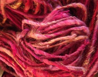 May include: A close-up of a bundle of pink and peach yarn with gold glitter thread woven throughout.