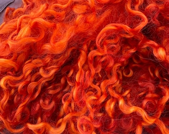 May include: A dense pile of vibrant orange and red curly fibre locks. The material features a mix of bright tangerine, deep crimson, and fiery orange tones with a distinct coiled texture throughout the entire mass of loose, soft, and wavy strands.