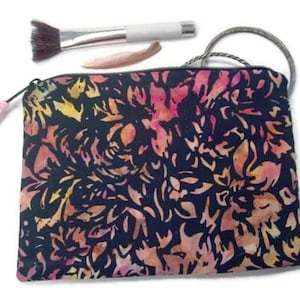 May include: A black zippered pouch with a pink tassel. The pouch is made of fabric with a floral pattern in shades of pink, orange, and yellow.
