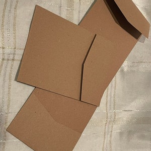 May include: Three brown paper envelopes of different sizes, stacked on top of each other. The envelopes are made of a textured, recycled paper.