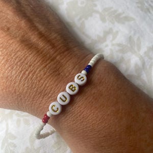 May include: White beaded bracelet with red and blue accents spelling out "CUBS" in gold letters.