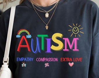 May include: Black t-shirt with a colorful "AUTISM" graphic and the words "Empathy, Compassion, Extra Love" printed below. The graphic includes a rainbow, a sun, and a heart.
