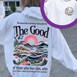 May include: White hoodie with a graphic on the back featuring the text "The Good" above a colourful landscape with a rainbow and floral elements. The front of the hoodie has a small floral design with a bird. The hoodie has long sleeves.