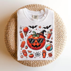 May include: A white t-shirt featuring a central graphic of a jack-o'-lantern tomato wearing sunglasses and a witch hat. Surrounding the tomato are summer and Halloween icons including ice cream, popsicles, a beach ball, flip-flops, and bats.