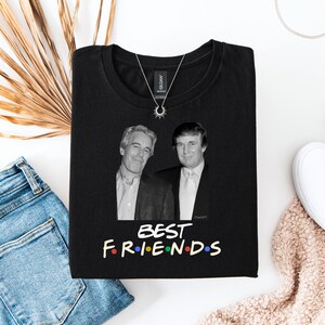 May include: Black t-shirt with a black and white image of two men. The text "BEST FRIENDS" is printed in colourful letters below the image. A silver necklace with a sun pendant is on the shirt.