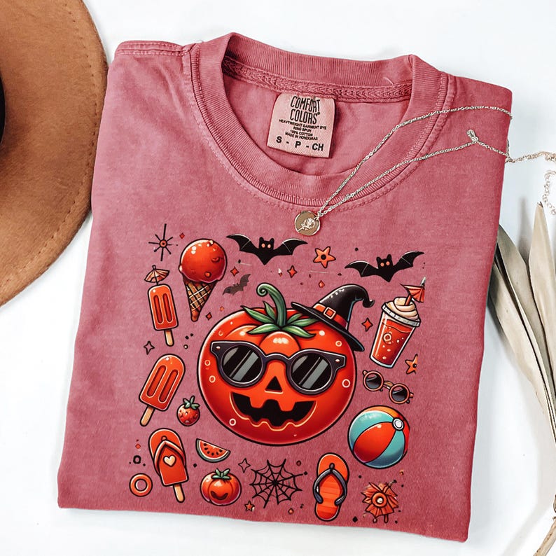May include: A dusty rose t-shirt with a Comfort Colors label in the collar. The graphic features a central jack-o'-lantern wearing sunglasses and a witch hat, surrounded by summer icons like ice cream, popsicles, flip-flops, and a beach ball.
