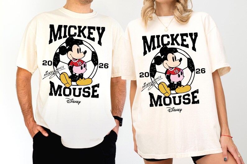 Puede incluir: Camisetas color crema con un gr&aacute;fico de Mickey Mouse. El dise&ntilde;o incluye a Mickey con uniforme de f&uacute;tbol, el texto "MICKEY MOUSE", el n&uacute;mero "26" y el logotipo de Disney. Las camisetas son de manga corta.