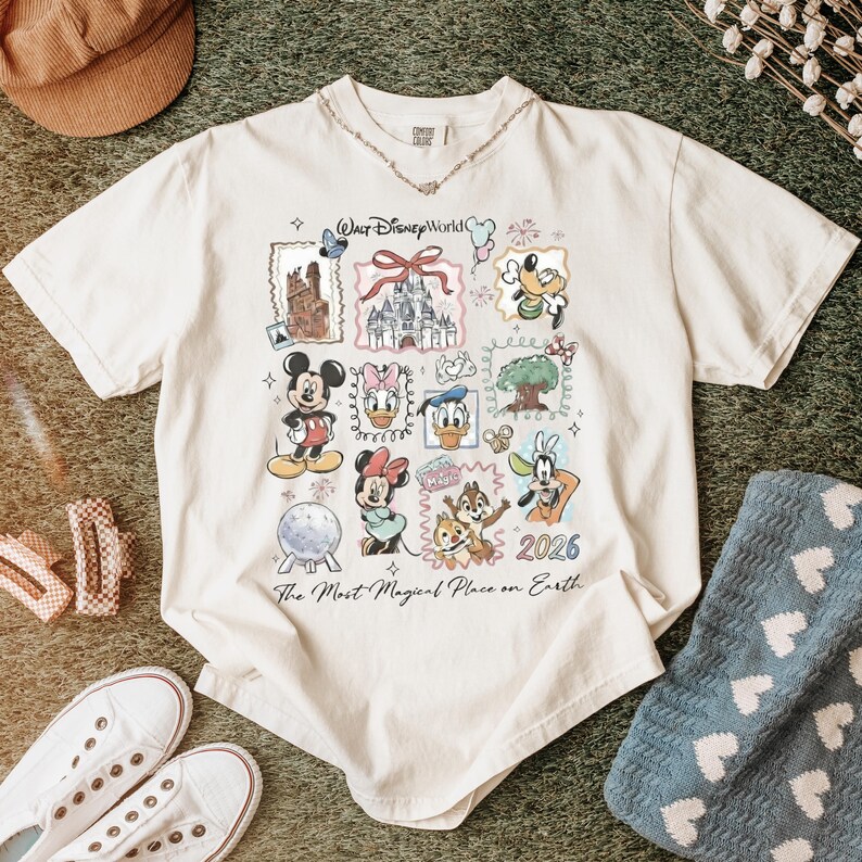 Puede incluir: Camiseta color crema con un gr&aacute;fico colorido de personajes y lugares emblem&aacute;ticos de Disney. El dise&ntilde;o incluye a Mickey Mouse, Minnie Mouse, Donald Duck y un castillo. Tambi&eacute;n se ve el texto "Walt Disney World" y "The Most Magical Place on Earth".