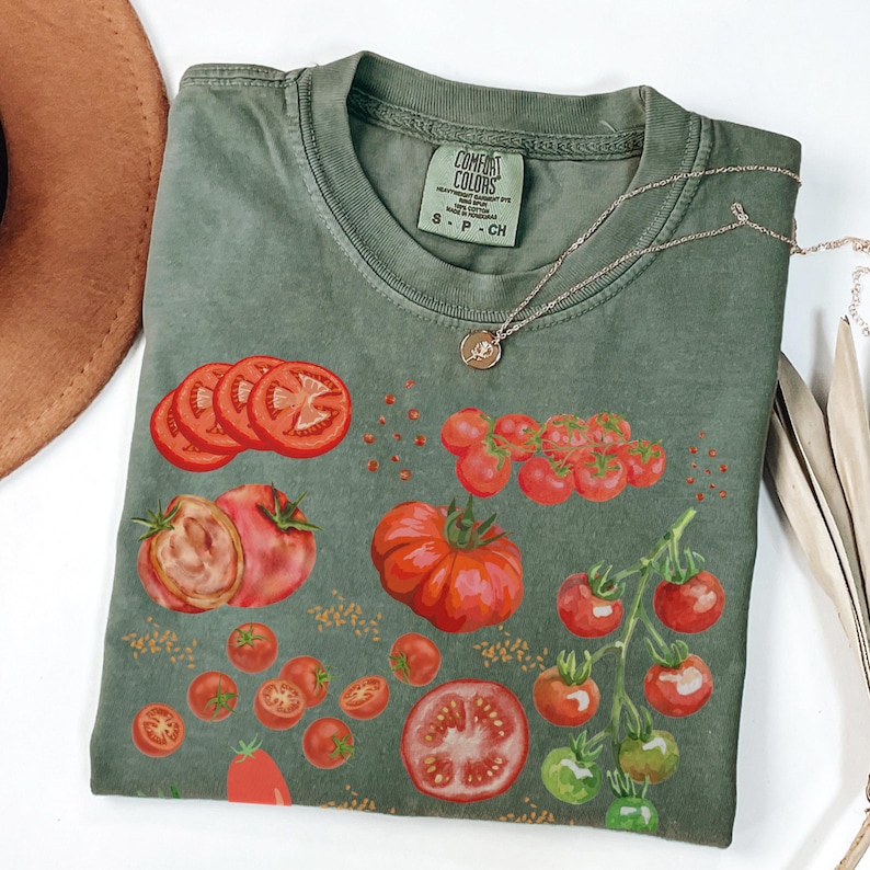 May include: A green t-shirt with a graphic print of red tomatoes. The shirt has the text "COMFORT COLORS" on the tag.