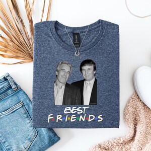 May include: A navy blue t-shirt with a black and white image of two men. The words "BEST FRIENDS" are written in colourful letters below the image. A silver necklace with a sun-shaped pendant is on the shirt.