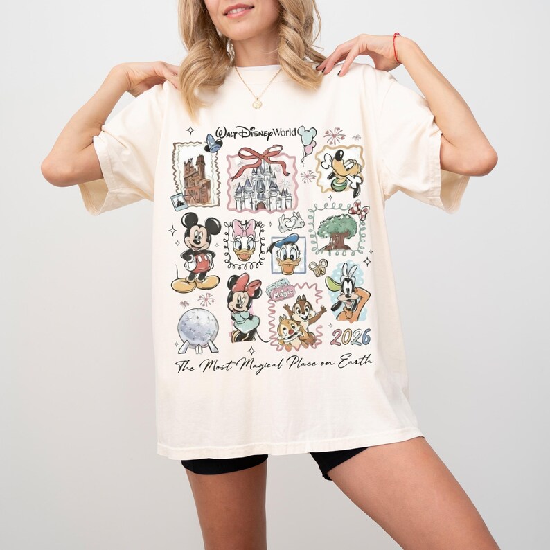 Puede incluir: Camiseta de color crema con un gr&aacute;fico colorido de varios personajes y lugares emblem&aacute;ticos de Disney. El dise&ntilde;o incluye a Mickey Mouse, Minnie Mouse, el Pato Donald y el castillo de Cenicienta. El texto en la camiseta dice "Walt Disney World" y "The Most Magical Place on Earth" con el a&ntilde;o "2026".