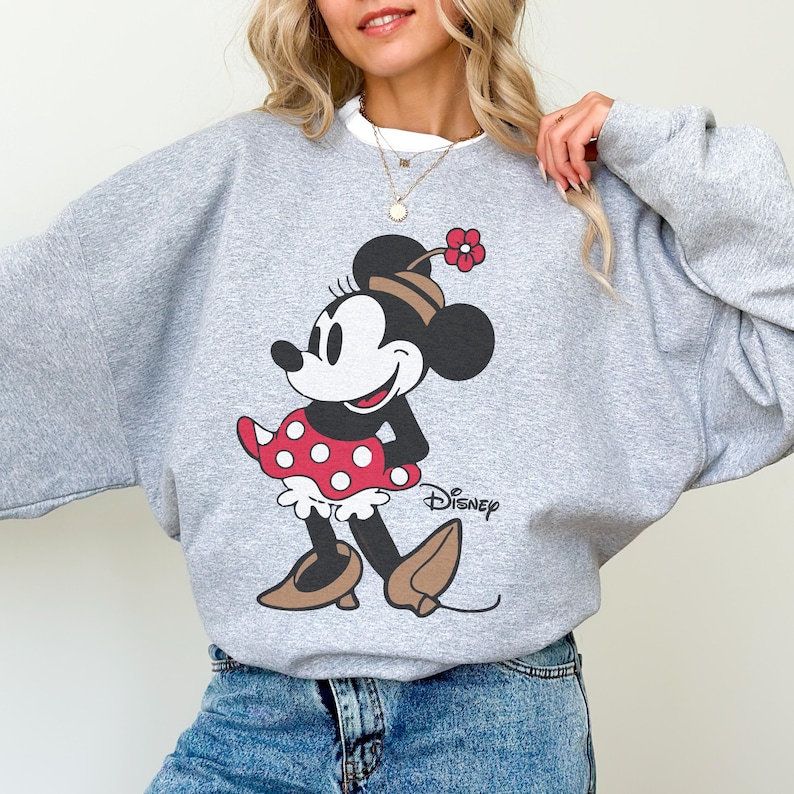 May include: A light grey sweatshirt with a Minnie Mouse graphic. The cartoon character is wearing a red polka dot dress, brown shoes, and a matching bow. The Disney logo is printed on the bottom right.