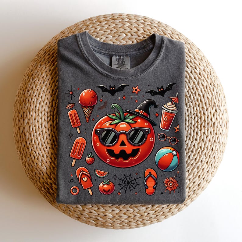 May include: A charcoal gray t-shirt featuring a graphic print of a jack-o'-lantern wearing sunglasses and a witch hat, surrounded by summer-themed icons including ice cream, popsicles, flip-flops, a beach ball, bats, and a spider web.