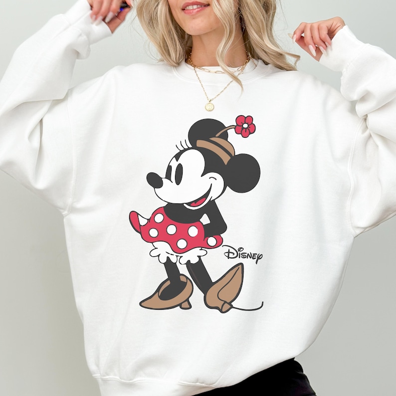 May include: White sweatshirt with a Minnie Mouse graphic. The cartoon character is shown in a red polka-dot dress, brown shoes, and a matching hat with a red flower. The Disney logo is printed below the character.