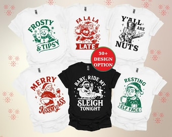 May include: A collection of white and black t-shirts with Christmas-themed graphics. Designs include a snowman, Santa Claus, a nutcracker, and an elf. Text includes "Frosty & Tipsy", "Fa La La Late", "Y'all are Nuts", "Merry Kissmyass", "Baby, Ride My Sleigh Tonight", and "Resting Elf Face".