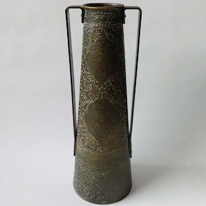 Peut inclure: Un vase en laiton haut avec deux poignées. Le vase présente un motif floral en relief complexe.