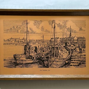 Puede incluir: Impresión en blanco y negro enmarcada de dos barcos de pesca atracados en un puerto. La obra de arte, titulada "The Harbour, Ayr", presenta un trabajo de línea detallado y está ambientada sobre un fondo beige dentro de un marco de madera.