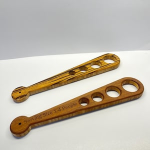 May include: Two wooden serving spoons with circular cutouts. One spoon is a light brown color with the text "Serving Size 1-4 People". The other spoon has a striped pattern and the text "Serving Size 1-4 People".
