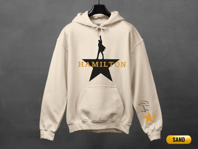 A white hoodie with a black silhouette of a person on a star and the word "HAMILTON" printed on it.