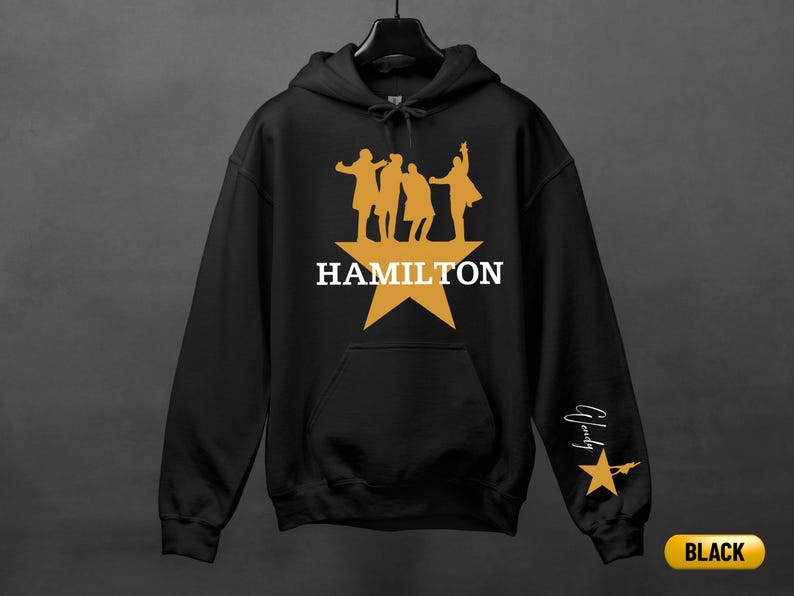 A black hoodie with a yellow star and silhouettes of three people, along with the text "HAMILTON" and a star.