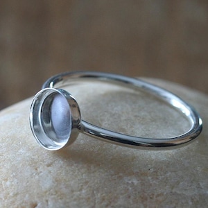 May include: A silver ring with a round bezel setting for a cabochon stone. The ring is simple and elegant, perfect for a minimalist look.