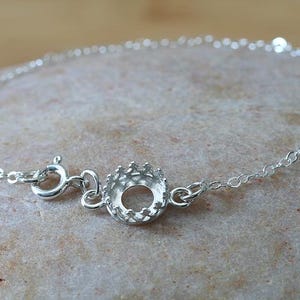 May include: A silver bracelet with a round bezel setting. The bracelet is made of a delicate chain and has a lobster clasp.