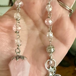 May include: Two hanging ornaments featuring silver-toned chains with faceted clear and pale pink beads. One chain ends in a smooth, pointed, light pink stone pendant with a silver cap, while the other features a silver filigree charm and heart.