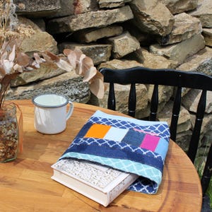 Könnte beinhalten: Ein Buchcover aus Jeans und anderen Stoffen in Blautönen, Orange, Pink und Weiß. Das Cover hat ein geometrisches Muster und ist zum Schutz eines Buches gedacht.