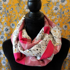Könnte beinhalten: Ein rosafarbener und weißer floral bedruckter Infinity-Schal mit einem rosafarbenen und weißen floralen Muster. Der Schal ist aus einem weichen, bequemen Stoff gefertigt und perfekt, um jedem Outfit einen Hauch von Stil zu verleihen.