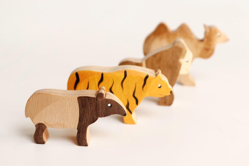 Puede incluir: Un conjunto de cuatro figuras de animales de madera dispuestas en fila. Las figuras incluyen un tapir de madera clara y oscura, un tigre amarillo con rayas negras, un gorila marr&oacute;n y un camello marr&oacute;n claro con dos jorobas en la espalda.
