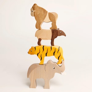 Puede incluir: Una pila vertical de cuatro figuras de animales de madera. En la base hay un elefante de color beige claro, coronado por un tigre amarillo con rayas negras, un tapir marr&oacute;n y beige, y un gorila marr&oacute;n claro en la parte superior. Cada figura es de madera.