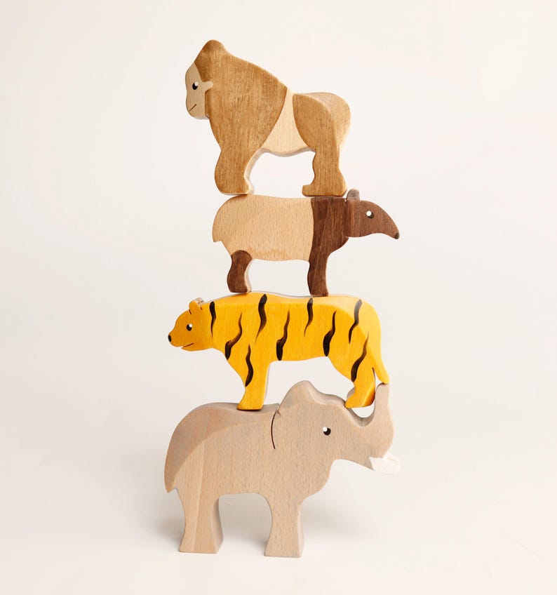 Puede incluir: Una pila vertical de cuatro figuras de animales de madera. En la base hay un elefante de color beige claro, coronado por un tigre amarillo con rayas negras, un tapir marr&oacute;n y beige, y un gorila marr&oacute;n claro en la parte superior. Cada figura es de madera.