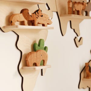 May include: Wooden world map wall decor with animal figurines. The map is made of light-coloured wood with dark brown edges. The shelves hold wooden animal toys, including a lion, tiger, rhino, and elephant.