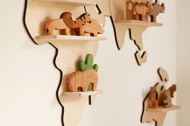May include: Wooden world map wall decor with animal figurines. The map is made of light-coloured wood with dark brown edges. The shelves hold wooden animal toys, including a lion, tiger, rhino, and elephant.