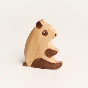 Puede incluir: Una figura de panda de madera clara con detalles en marr&oacute;n oscuro en las orejas, los parches de los ojos, las extremidades y la base. La figura del animal est&aacute; representada en posici&oacute;n sentada con un acabado liso y veta de madera visible.